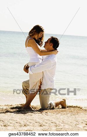 Side profile of a young woman and a mid adult man embracing each other on the beach View Large Photo Image Stock Image - Side profile of a young woman and a mid adult man embracing each other on the beach. Fotosearch