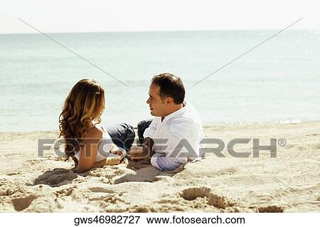 Stock Photo - Side profile of a young woman and a mid adult man lying on the beach. Fotosearch