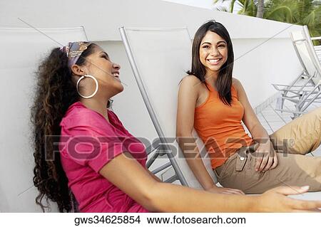 Side profile of a young woman and a teenage girl sitting on lounge chairs and smiling View Large Photo Image Picture - Side profile of a young woman and a teenage girl sitting on lounge chairs and smiling. Fotosearch