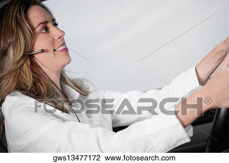Stock Image - Side profile of a young woman driving a car and wearing a hands free device. Fotosearch
