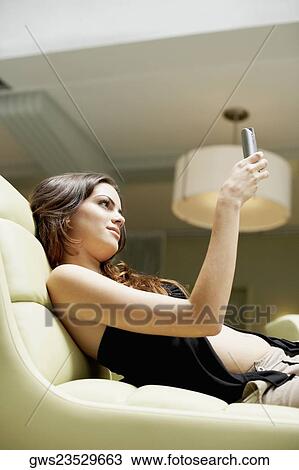 Stock Image - Side profile of a young woman reclining on a couch and holding a mobile phone. Fotosearch