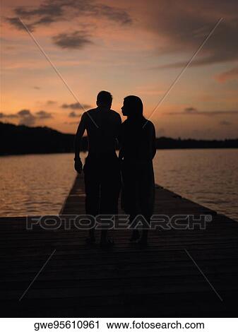 Silhouette of a man and a woman walking on a pier View Large Photo Image Stock Image - Silhouette of a man and a woman walking on a pier. Fotosearch