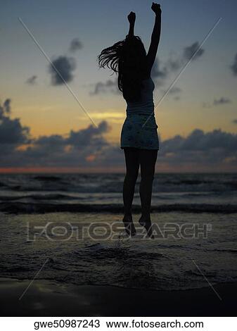 Stock Image - Silhouette of a teenage girl jumping on the beach at dusk. Fotosearch