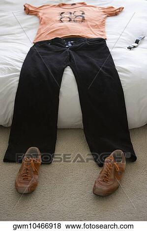 Stock Photo - T-shirt and jeans on the bed with a pair of shoes on the floor. Fotosearch