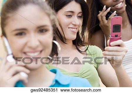 Teenage girl looking at a mobile phone with two other teenage girls talking on mobile phones View Large Photo Image Stock Image - Teenage girl looking at a mobile phone with two other teenage girls talking on mobile phones. Fotosearch