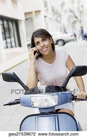 Teenage girl riding on a motor scooter and talking on mobile phone View Large Photo Image Stock Image - Teenage girl riding on a motor scooter and talking on mobile phone. Fotosearch