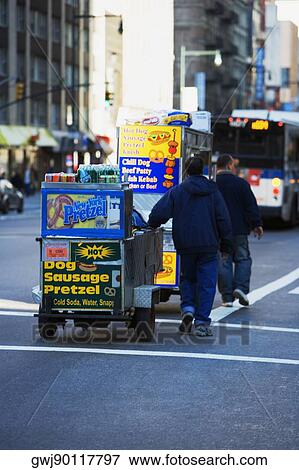 Stock Photo - Two men pulling a hot dog stand, Manhattan, New York City, New York State, USA. Fotosearch