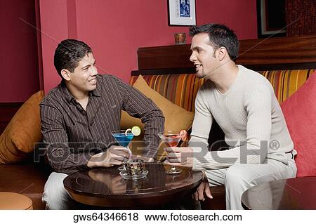 Young man and a mid adult man sitting on a couch holding cocktails View Large Photo Image Stock Photo - Young man and a mid adult man sitting on a couch holding cocktails. Fotosearch