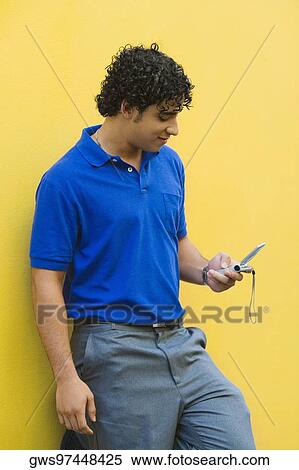 Young man leaning against the wall and using a mobile phone View Large Photo Image Stock Photography - Young man leaning against the wall and using a mobile phone. Fotosearch