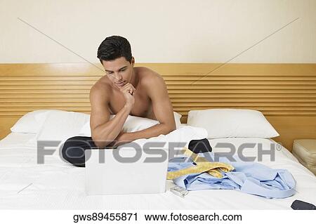 Young man sitting on the bed with a laptop View Large Photo Image Stock Image - Young man sitting on the bed with a laptop. Fotosearch