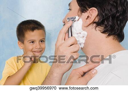 Stock Image - Boy looking at his father shaving in the bathroom. Fotosearch