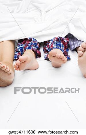 Stock Photo - Close-up of a couple's feet with their child on the bed. Fotosearch
