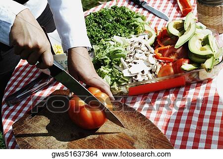 Picture - Close-up of a person's hand cutting a tomato with a kitchen knife. Fotosearch