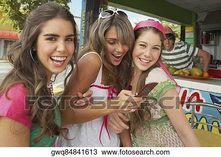 Stock Image - Close-up of a teenage girl holding a mobile phone and standing at the juice bar with her friends. Fotosearch