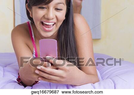 Close-up of a teenage girl lying on the bed and text messaging on a mobile phone View Large Photo Image Stock Photo - Close-up of a teenage girl lying on the bed and text messaging on a mobile phone. Fotosearch