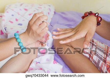 Picture - Close-up of a woman's hand applying nail polish on another woman's hand. Fotosearch