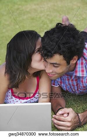 Stock Image - Close-up of a young couple lying in a lawn in front of a laptop. Fotosearch