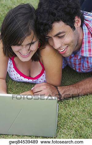 Close-up of a young couple lying in a lawn in front of a laptop View Large Photo Image Stock Photo - Close-up of a young couple lying in a lawn in front of a laptop. Fotosearch