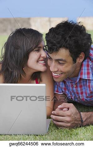Stock Photograph - Close-up of a young couple lying in a lawn in front of a laptop. Fotosearch