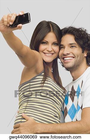 Close-up of a young couple taking a photograph of themselves with a mobile phone View Large Photo Image Stock Photo - Close-up of a young couple taking a photograph of themselves with a mobile phone. Fotosearch