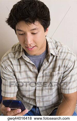 Close-up of a young man holding a mobile phone and text messaging View Large Photo Image Stock Photo - Close-up of a young man holding a mobile phone and text messaging. Fotosearch