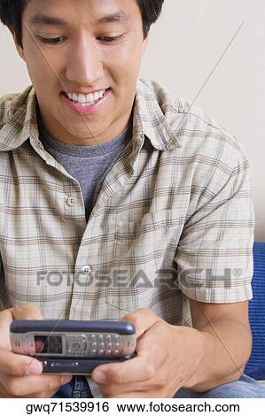 Stock Photograph - Close-up of a young man holding a mobile phone and text messaging. Fotosearch