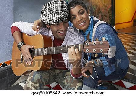 Stock Image - Close-up of a young man playing a guitar and smiling with a young woman. Fotosearch