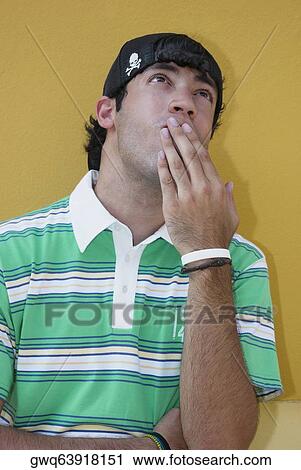 Stock Image - Close-up of a young man with his hands covering his mouth. Fotosearch