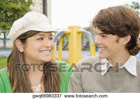 Stock Photo - Close-up of a young woman and a teenage boy looking at each other and smiling. Fotosearch