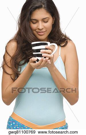 Close-up of a young woman holding a mug of coffee and smiling View Large Photo Image Stock Photo - Close-up of a young woman holding a mug of coffee and smiling. Fotosearch