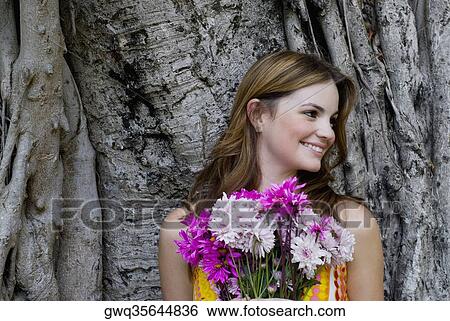 Close-up of a young woman holding a bouquet of flowers and looking away View Large Photo Image Stock Photograph - Close-up of a young woman holding a bouquet of flowers and looking away. Fotosearch