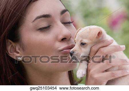 Picture - Close-up of a young woman kissing a puppy. Fotosearch