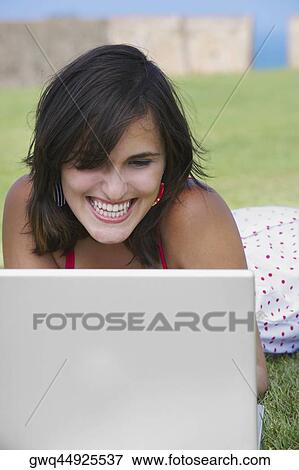 Close-up of a young woman lying in a lawn in front of a laptop View Large Photo Image Stock Photo - Close-up of a young woman lying in a lawn in front of a laptop. Fotosearch