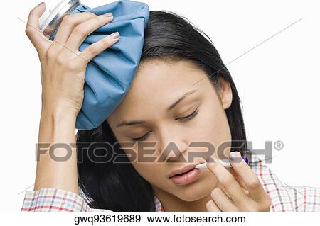 Stock Photo - Close-up of a young woman measuring her temperature with a thermometer and holding an ice pack on her head. Fotosearch