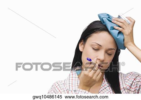 Stock Photography - Close-up of a young woman measuring her temperature with a thermometer and holding an ice pack on her head. Fotosearch