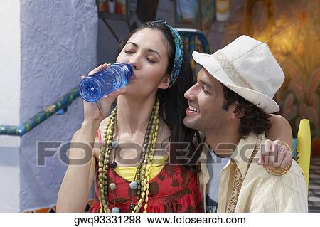 Close-up of a young woman sitting with a young man and drinking water from a water bottle View Large Photo Image Stock Photo - Close-up of a young woman sitting with a young man and drinking water from a water bottle. Fotosearch