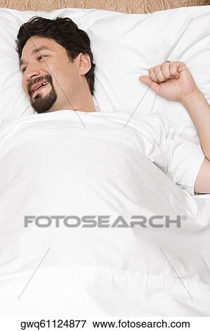 Stock Photo - High angle view of a mid adult man lying on the bed and smiling. Fotosearch