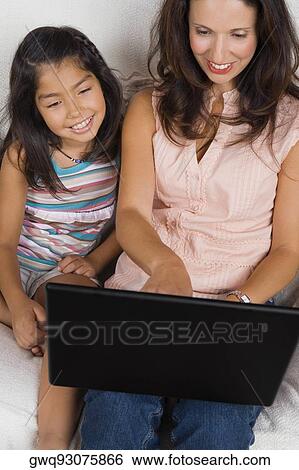 High angle view of a mid adult woman using a laptop with her daughter sitting beside her and smiling View Large Photo Image Stock Photograph - High angle view of a mid adult woman using a laptop with her daughter sitting beside her and smiling. Fotosearch