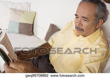High angle view of a senior man sitting on a couch and holding a book View Large Photo Image Stock Image - High angle view of a senior man sitting on a couch and holding a book. Fotosearch