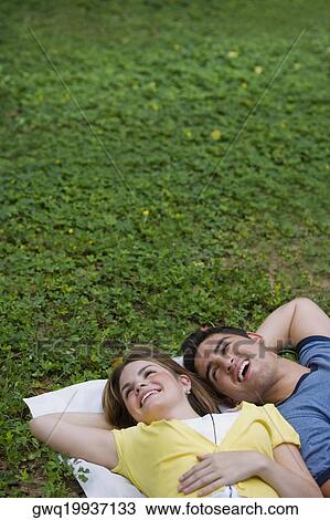 Stock Image - High angle view of a young couple lying in a park and smiling. Fotosearch