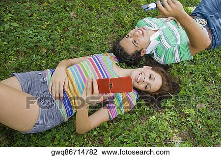 High angle view of a young couple lying in park and holding a mobile phone View Large Photo Image Stock Image - High angle view of a young couple lying in park and holding a mobile phone. Fotosearch