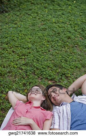 Stock Photo - High angle view of a young couple lying in a park and smiling. Fotosearch