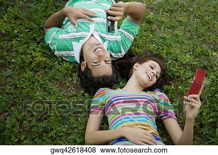 High angle view of a young couple lying in a park and using mobile phones View Large Photo Image Stock Photo - High angle view of a young couple lying in a park and using mobile phones. Fotosearch