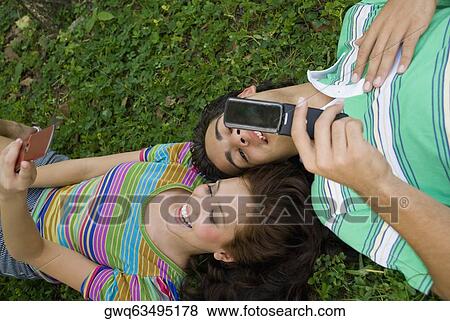 High angle view of a young couple lying in a park and holding mobile phones View Large Photo Image Stock Photo - High angle view of a young couple lying in a park and holding mobile phones. Fotosearch