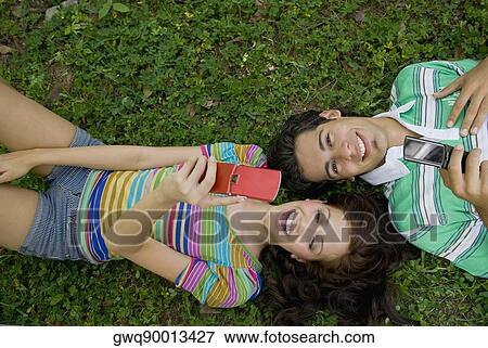 High angle view of a young couple lying in a park and holding mobile phones View Large Photo Image Stock Photo - High angle view of a young couple lying in a park and holding mobile phones. Fotosearch