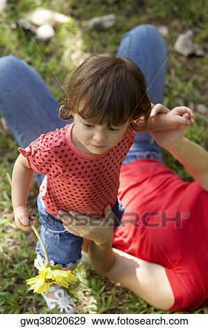 Stock Photo - High angle view of a young woman lying on grass and holding her daughter. Fotosearch
