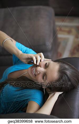 High angle view of a young woman lying on a couch and talking on a mobile phone View Large Photo Image Stock Photo - High angle view of a young woman lying on a couch and talking on a mobile phone. Fotosearch