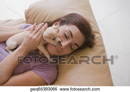 Stock Photograph - High angle view of a young woman lying on a couch and hugging a puppy. Fotosearch