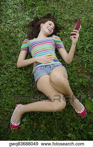 Stock Photo - High angle view of a young woman holding a mobile phone and laughing. Fotosearch