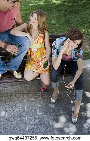 High angle view of a young woman listening to music with her friends sitting beside her View Large Photo Image Stock Photography - High angle view of a young woman listening to music with her friends sitting beside her. Fotosearch